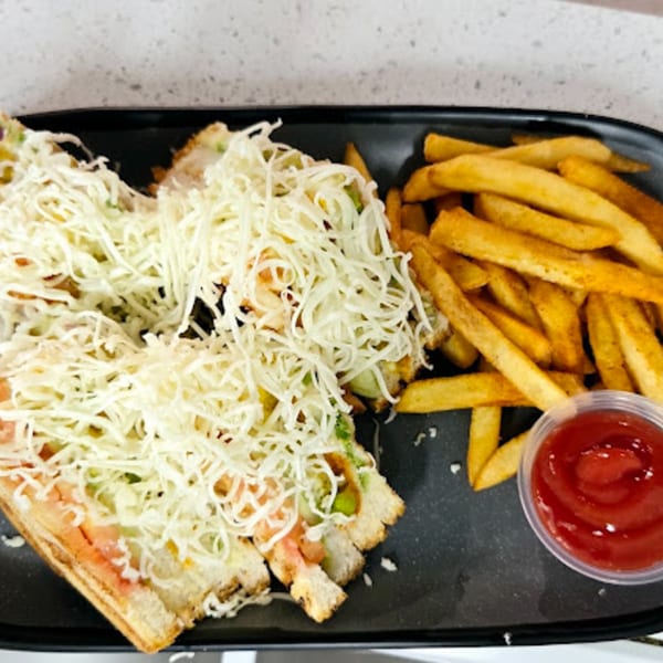 Indian vegetarian sandwich with shredded cheese, served with golden fries and ketchup on a black plate.
