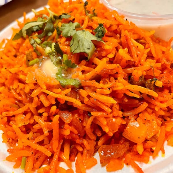 Close-up of vibrant orange Indian rice, garnished with fresh cilantro and a dollop of butter.