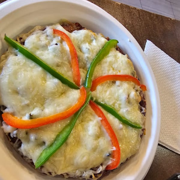 A round Indian vegetarian dish topped with melted cheese and strips of red and green bell peppers.