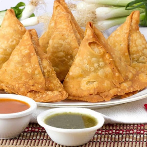A plate of golden-brown Indian samosas with two dipping sauces and green onions.