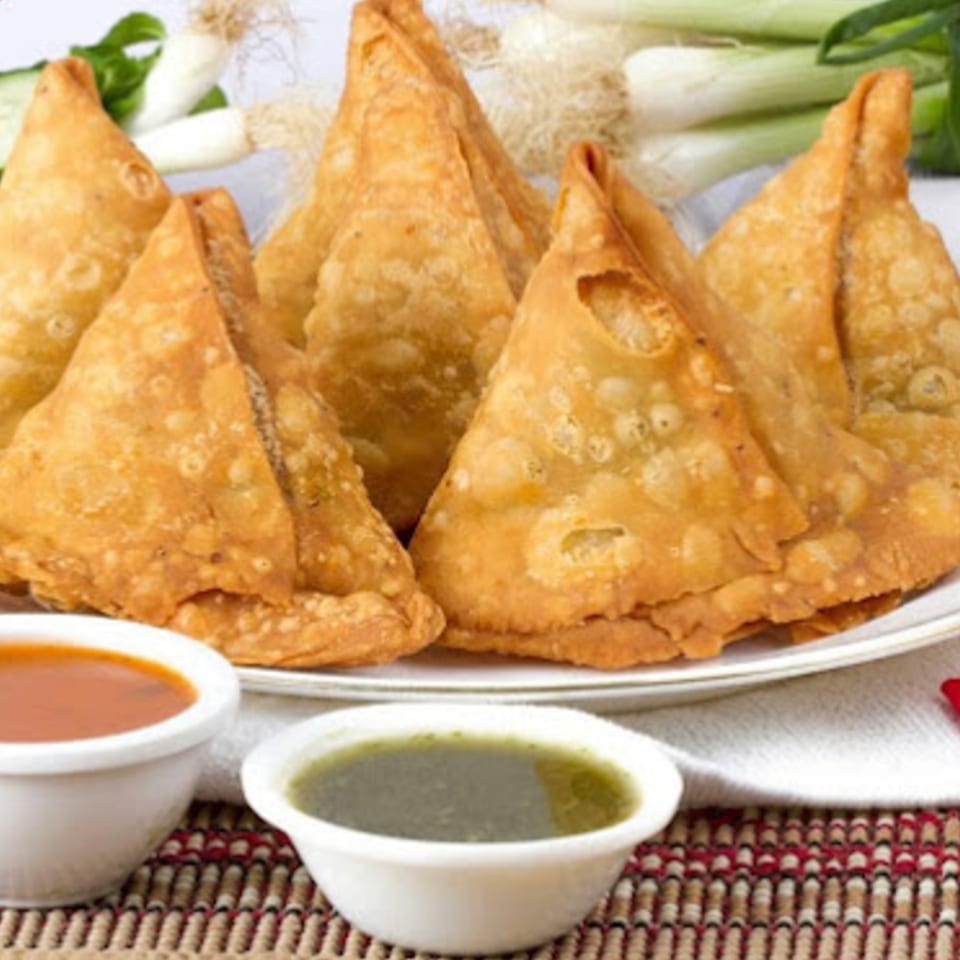 A plate of golden-brown Indian samosas with two dipping sauces and green onions.