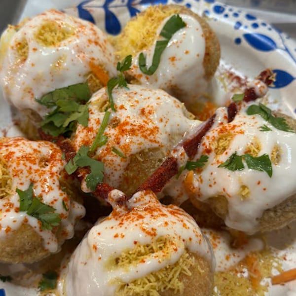 Close-up of Indian dahi puri, topped with yogurt, red chili powder, sev, and cilantro.