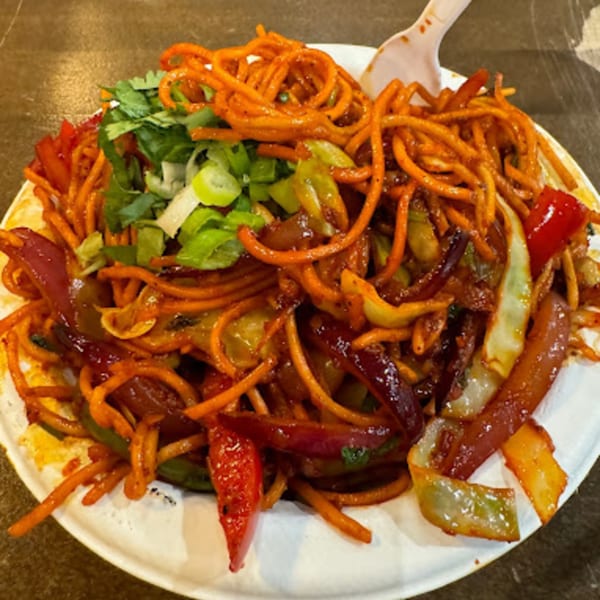 Close-up of Indian vegetarian noodles with red peppers, cabbage, and green onions on a white plate.