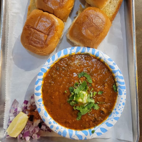 Pav Bhaji, an Indian vegetable curry, served with buttered buns, chopped onions, and a lemon wedge.